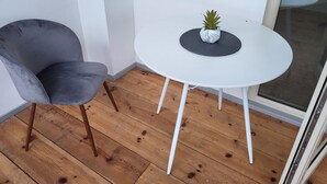 Pieni parveke, jossa on valkoinen pöytä, harmaa tuoli ja ruukussa oleva kasvi.