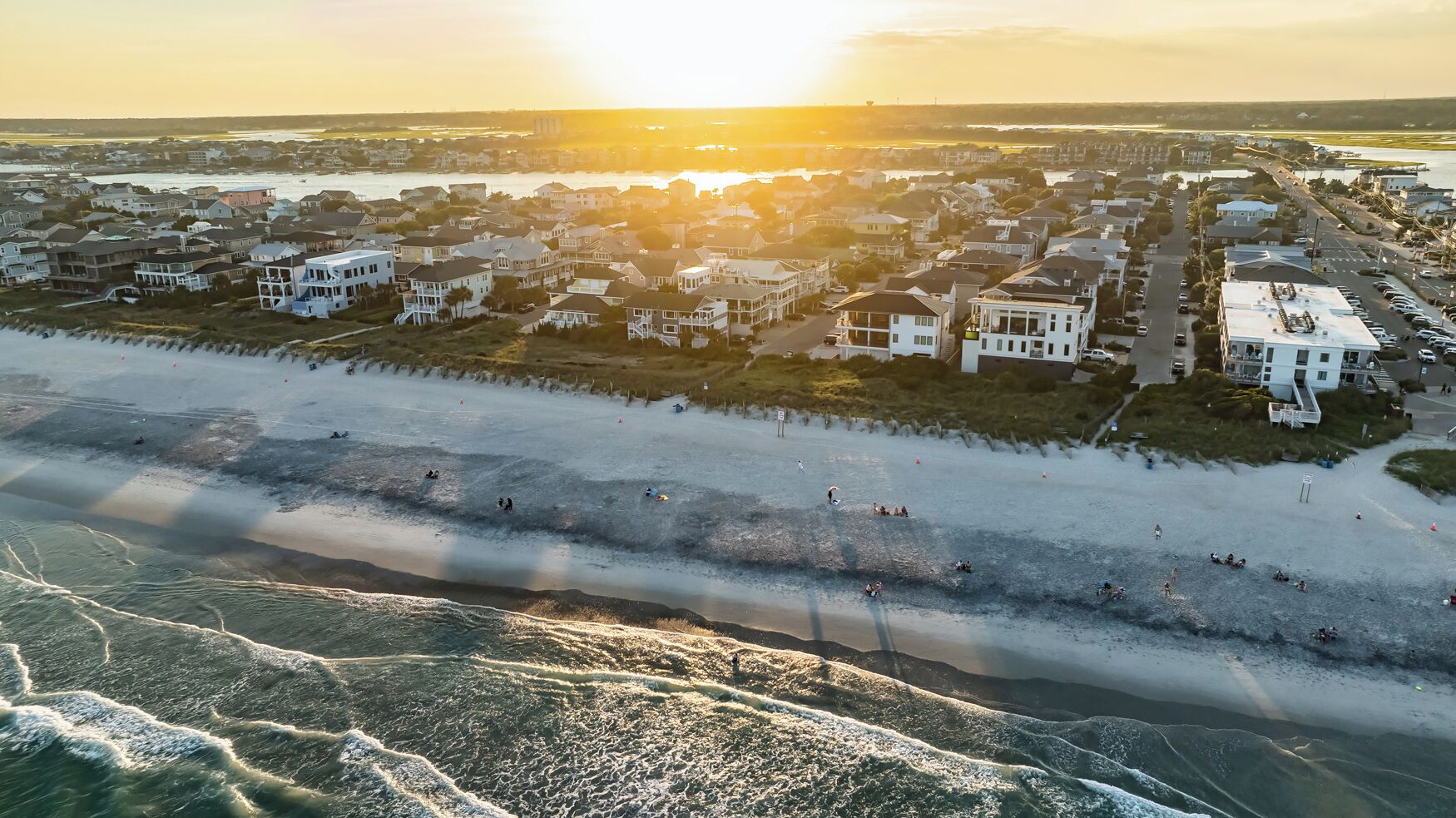Vista aérea de una zona residencial costera con casas a lo largo de la playa, una playa de arena y olas acercándose a la orilla.