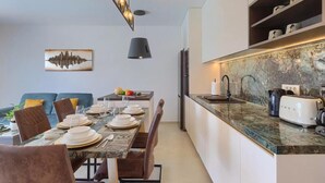 A modern kitchen with a marble countertop, a dining area with a set table, and a sofa in the background.