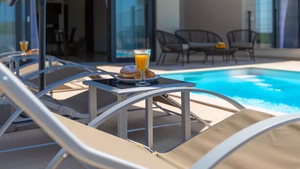 A poolside area with lounge chairs, a table with a drink and pastry, and a glass of orange juice.