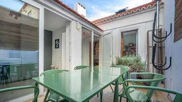 Une terrasse avec une table et des chaises en verre, un toit en tuiles et un espace jardin agrémenté de plantes.