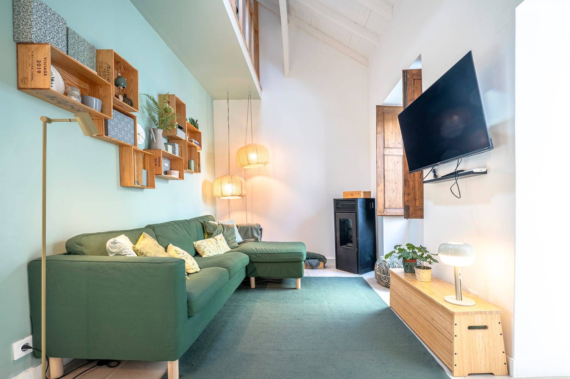 Un salon avec un canapé vert, des étagères en bois, un téléviseur à écran plat et une cheminée.