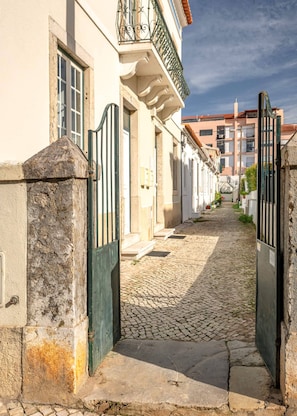 Una calle empedrada flanqueada por edificios de arquitectura tradicional, una entrada con portón y un cielo despejado.