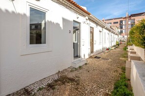 A narrow cobblestone street flanked by white buildings with doors and windows, leading to a staircase.