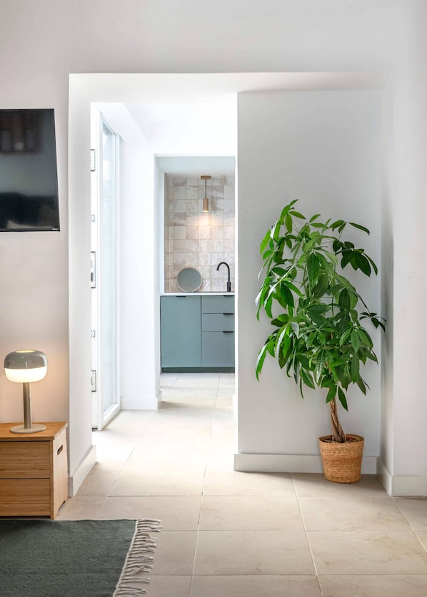 A hallway with a potted plant, a lamp, and a view into a kitchen area.