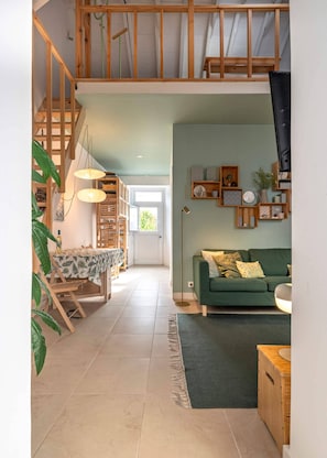 A spacious living area with a staircase, a dining table, a sofa, and a kitchen area.