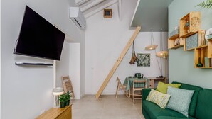 En moderne stue med en grøn sofa, træhylder, et fladskærms-tv og et spiseområde med et bord og stole.