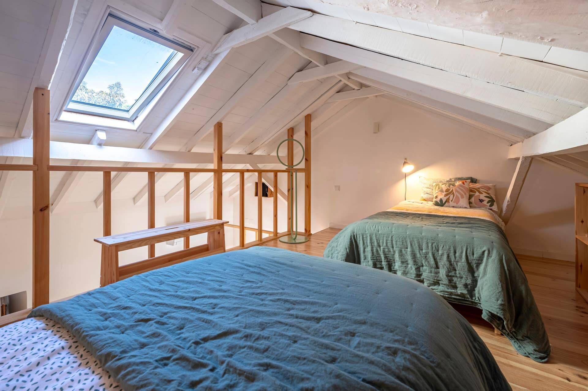 Een kamer met een schuine kap, dakraam, een bed met een groene dekbedovertrek, nachtkastje en een lamp.