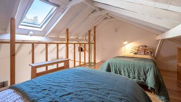 Een kamer met een schuine kap, dakraam, een bed met een groene dekbedovertrek, nachtkastje en een lamp.