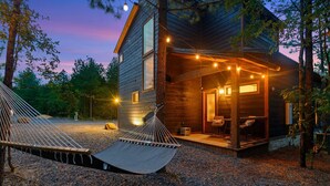 A modern log cabin with a hammock and string lights, surrounded by trees. - Sip and Stay Hideaway (Broken Bow)