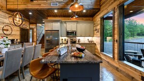 A modern kitchen with granite countertops, stainless steel appliances, and a large island with bar stools. - Sip and Stay Hideaway (Broken Bow)