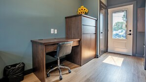 Quarto com escrivaninha de madeira, uma cadeira, lixeira e porta que dá para o exterior.