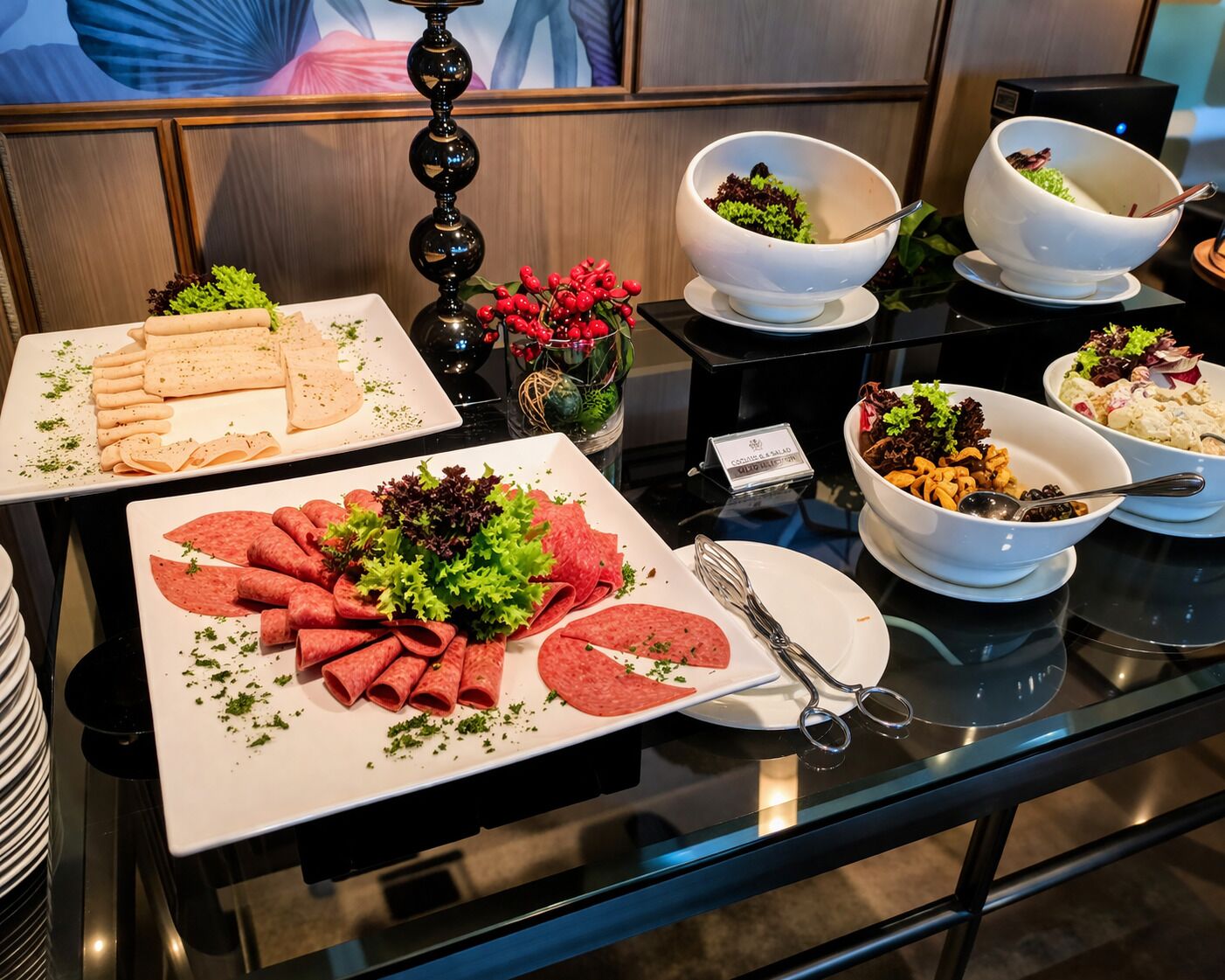 A buffet table with various food items including sliced meats, salads, and a decorative vase with red berries.