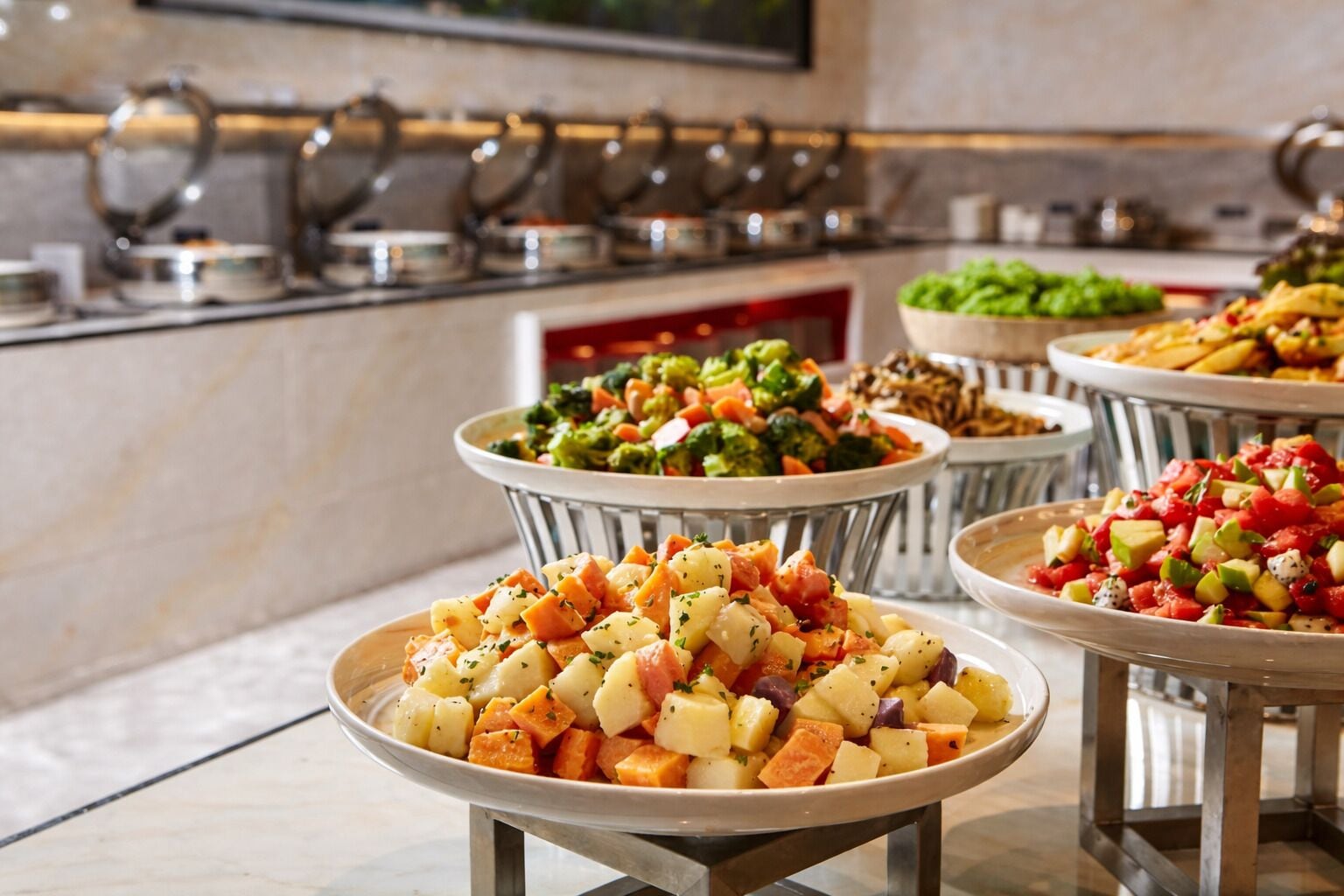 A buffet with various dishes, including a vegetable salad, a fruit salad, and other prepared foods.