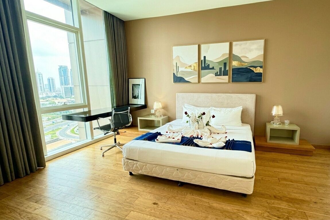 A hotel room with a large window, a bed with white linens, a desk, and a chair.