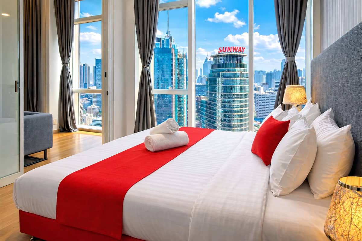 A hotel room with a large bed, red and white bedding, a city view, and a 'SUNWAY' building in the background.