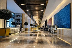 A modern hotel lobby with a reception desk, seating area, and large artwork on the walls.