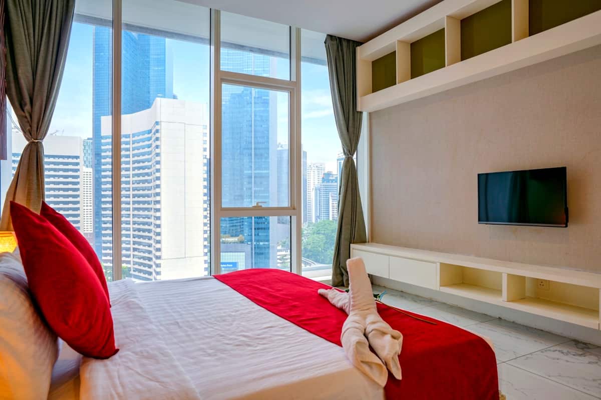 A hotel room with a large bed, a flat-screen TV, a city view, and a built-in shelf.