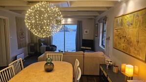 A cozy living room with a large window overlooking a body of water, a round dining table with chairs, a sofa, and a decorative light fixture. - Cottage 2 meters from the sea, 2 hours from Bergen in Norway. Unike location (Vestland)