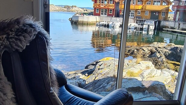 A room with a large sliding glass door leading to a waterfront view, a leather chair with a fur throw, and wooden flooring. - Cottage 2 meters from the sea, 2 hours from Bergen in Norway. Unike location (Vestland)