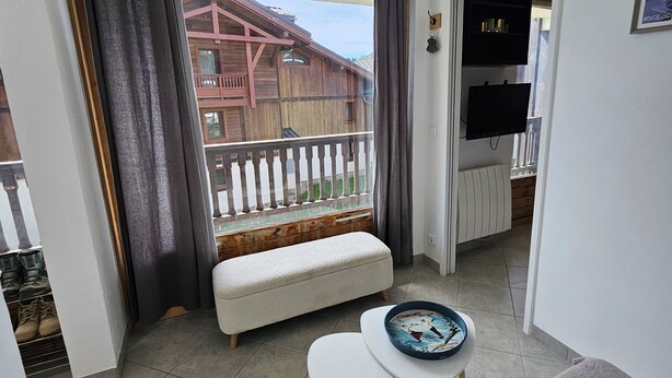 A balcony with a wooden railing, a white cushioned bench, and a view of a wooden building.