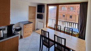 A compact kitchen with a dining table and chairs, a coffee maker, and a view of a balcony with a building in the background.