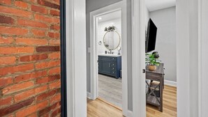 Un couloir menant à une salle de bain équipée d’un miroir, d’un lavabo et d’une plante en pot.