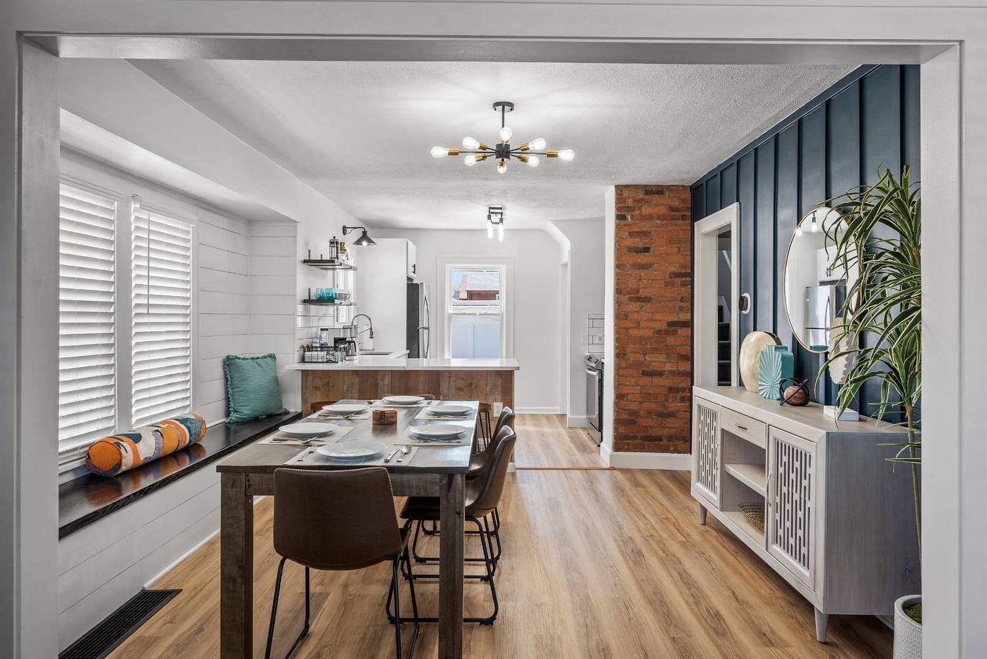A modern kitchen with a dining area, featuring a brick accent wall, white cabinetry, and a central island with a sink.