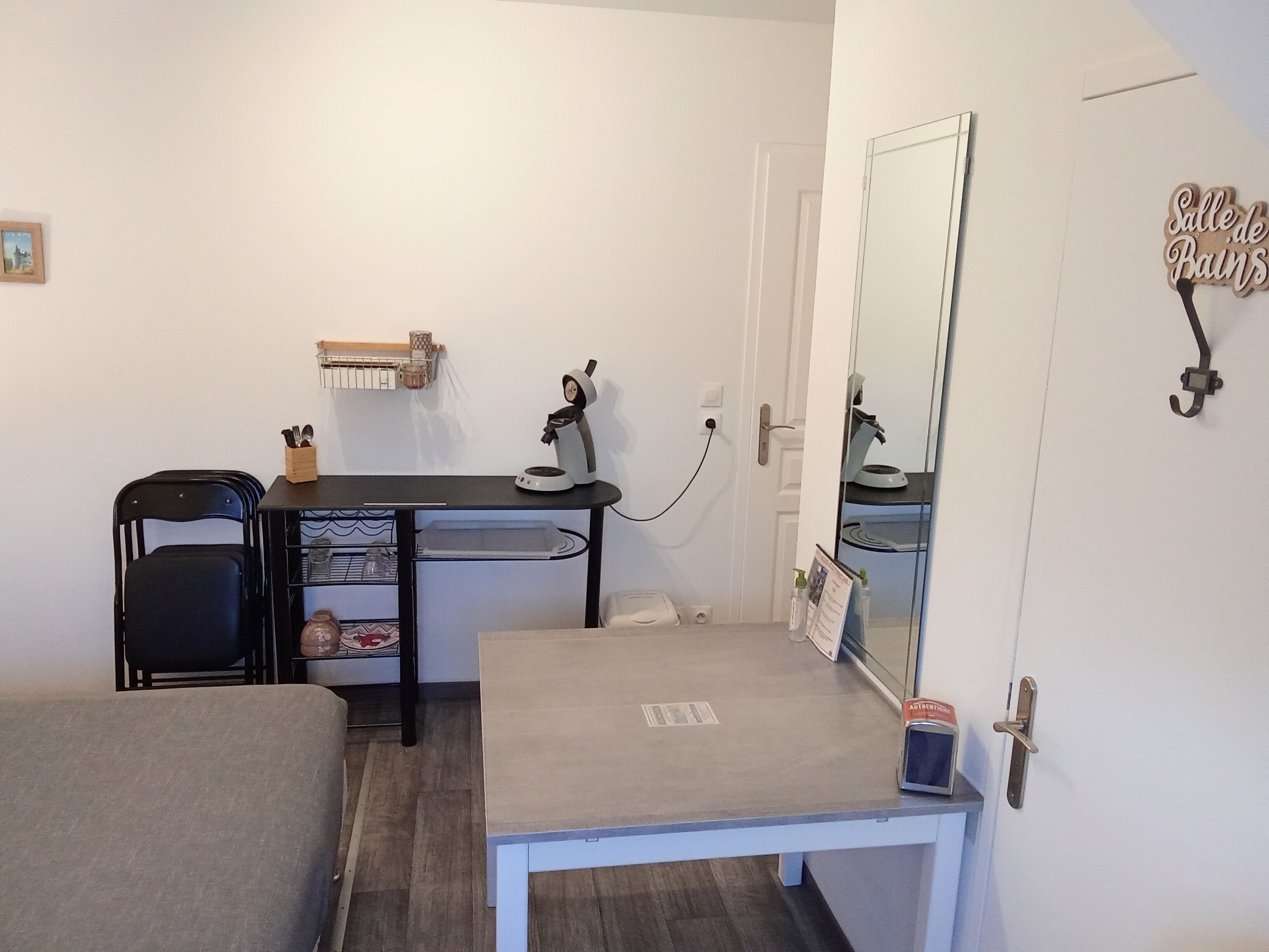 Une petite pièce avec un bureau, une chaise et un miroir. Il y a une porte avec une pancarte au-dessus.