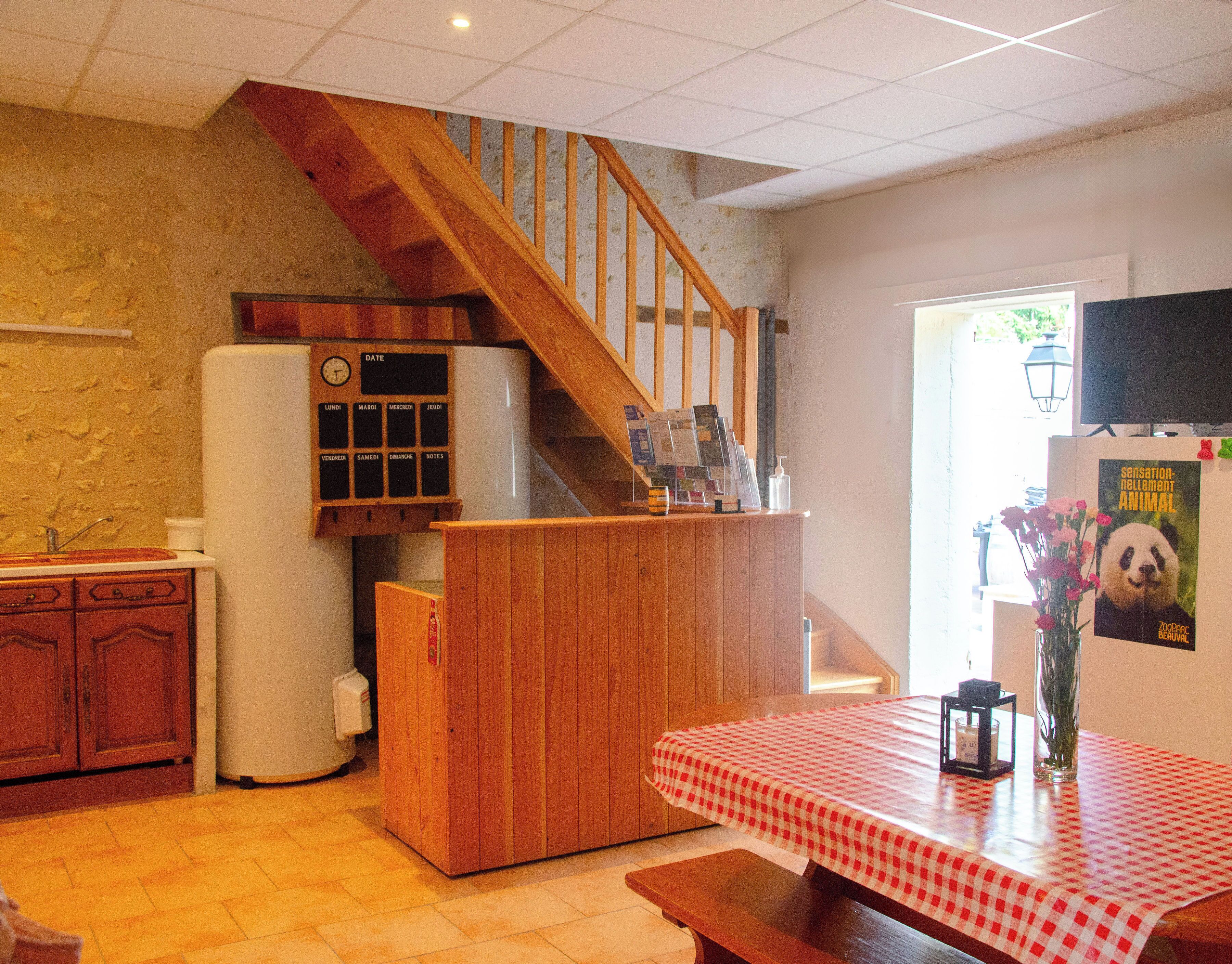 A kitchen with a wooden staircase, a refrigerator, a wooden counter, and a table with a checkered tablecloth.