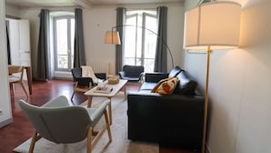 Een moderne woonkamer met een bank, stoelen, een salontafel en een lamp.