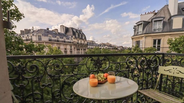 Een balkon met een tafel, gedekt met fruit en sap, met uitzicht op een stadsgezicht vol historische gebouwen.