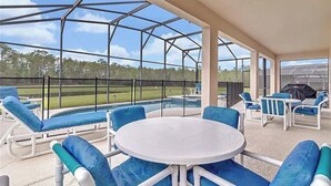 Un espacio al aire libre cubierto con piscina, sillas azules acolchadas y una mesa.