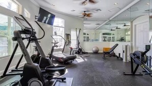 Gimnasio con máquinas de cardio, un espejo y un ventilador de techo.