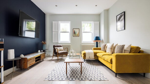 A modern living room with a yellow sofa, a coffee table, and a TV mounted on the wall. - The East Dulwich House (London)