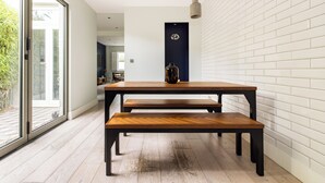 A modern dining area with a wooden table and benches, a dark door, and a white brick wall. - The East Dulwich House (London)