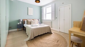 A bedroom with a bed, bedside table, lamp, and a large window. - The East Dulwich House (London)
