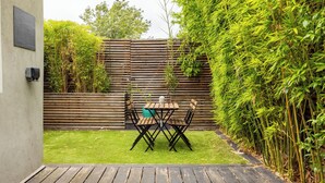 A patio with a table and chairs, a wooden deck, and a bamboo fence. - The East Dulwich House (London)