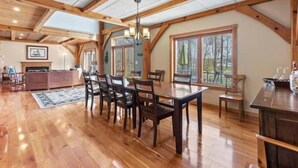 A spacious dining area with a wooden table and chairs, large windows, and a high ceiling with exposed beams. - Lakefront Cabin Boat slip Wifi Fishing Firepit (Orange)