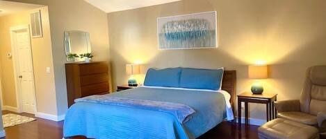 A bedroom with a bed, a ceiling fan, two bedside lamps, a chair, and a door.
