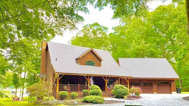 A wooden cabin with a porch, surrounded by lush greenery and a gravel driveway. - Lakefront Cabin Boat slip Wifi Fishing Firepit (Orange)