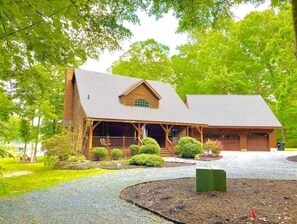 Guests can enjoy a serene atmosphere on the covered porch of this charming cabin, surrounded by lush greenery and well-maintained lawns.