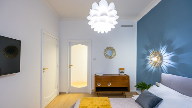 Une chambre à coucher comprenant un lit, une commode en bois, un luminaire fixé au mur et une porte dotée d’un panneau en verre dépoli.