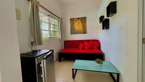 A compact living space with a kitchenette, a red sofa, a glass table, and a painting on the wall.