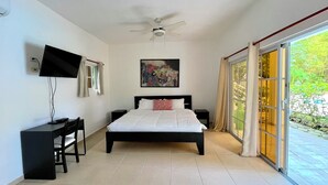 A bedroom with a bed, a desk, a television, a ceiling fan, and a large window.
