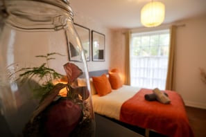 A room with a bed, a glass vase with plants, and a window with a view. - Designer apartment in modern neighborhood - 15 minutes from central London (London)
