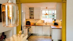A compact kitchen with white cabinets, a tiled floor, a window with curtains, and a hanging light fixture. - Designer apartment in modern neighborhood - 15 minutes from central London (London)