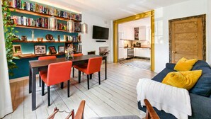 A modern living room with a dining area, a kitchen, and a cozy seating area with a sofa and cushions. - Designer apartment in modern neighborhood - 15 minutes from central London (London)