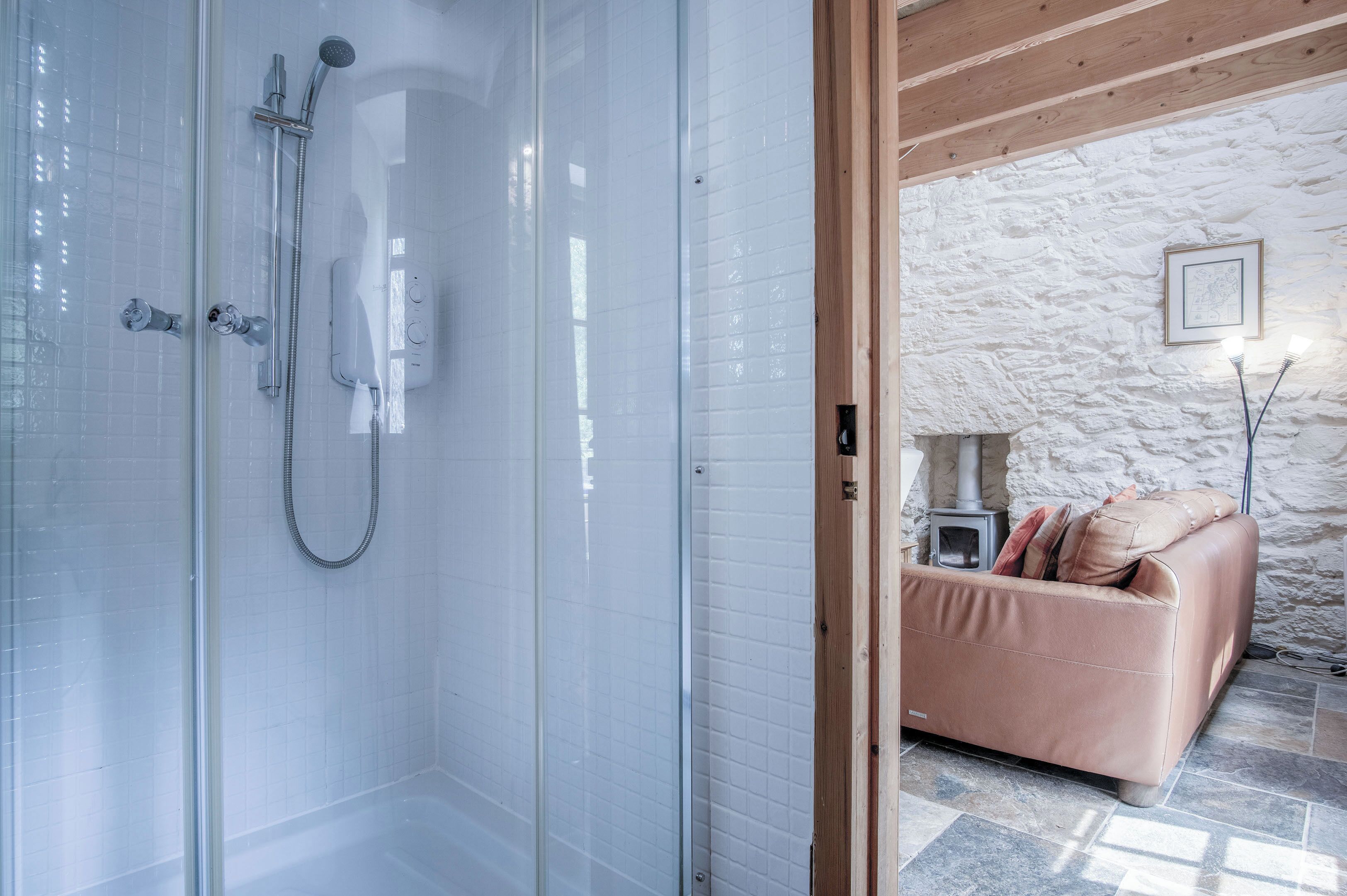 A modern bathroom with a glass shower enclosure, a beige sofa, and a stone wall.