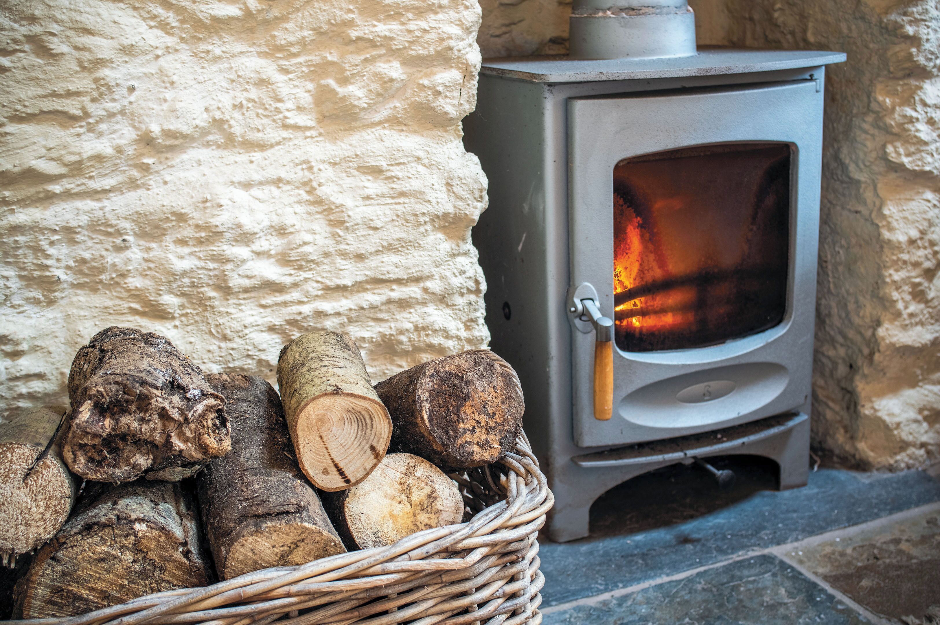 A stone wall with a wood-burning stove and a basket of logs.
